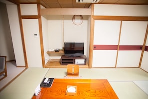 Perinteinen japanilainen huone, jossa on tatamimatto, televisio puisen jalustan päällä, pieni pöytä tarjottimella ja liukuovi.