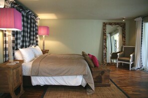 Une chambre d’hôtel avec un grand lit, une table de chevet en bois, une chaise, un miroir et une fenêtre avec des rideaux.