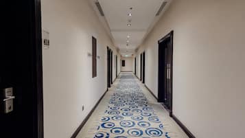 A hotel hallway with a patterned carpet, doors on both sides, and a number sign on the wall.