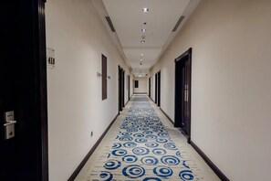 A hotel hallway with a patterned carpet, doors on both sides, and a number sign on the wall. - Doha Central Plaza Hotel (Doha)