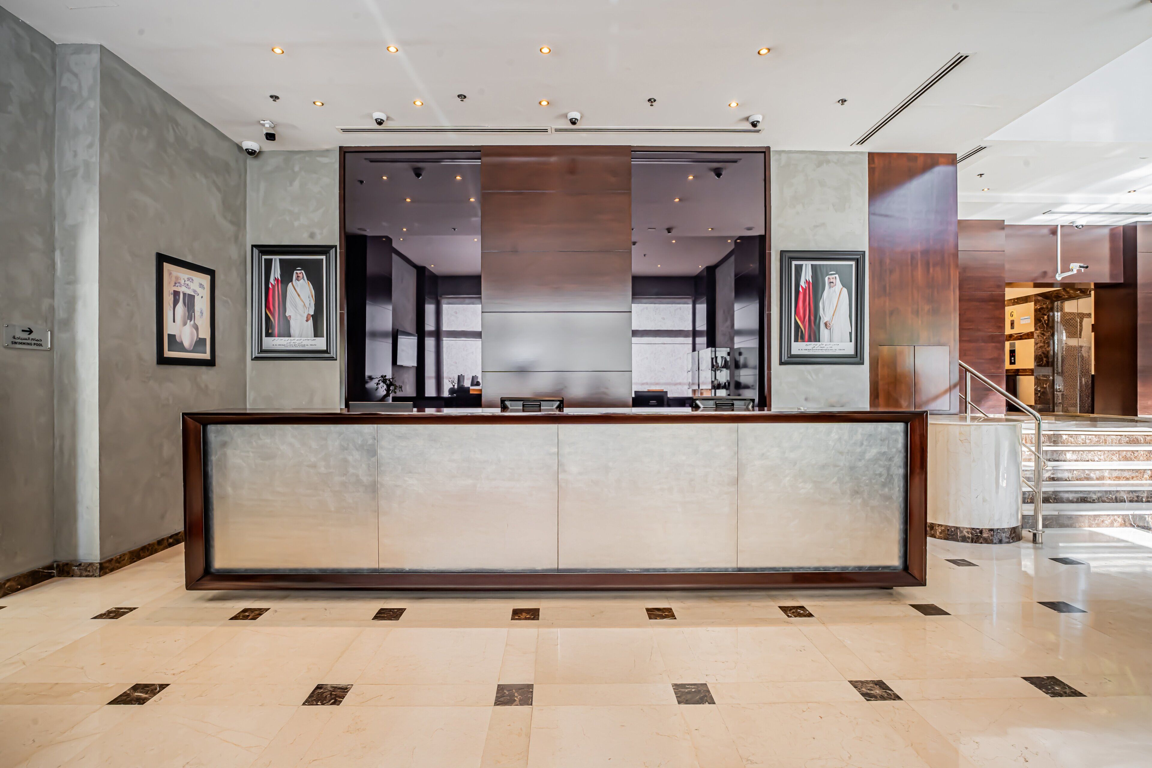 A reception area with a marble floor, framed portraits, and a staircase leading to an upper level.