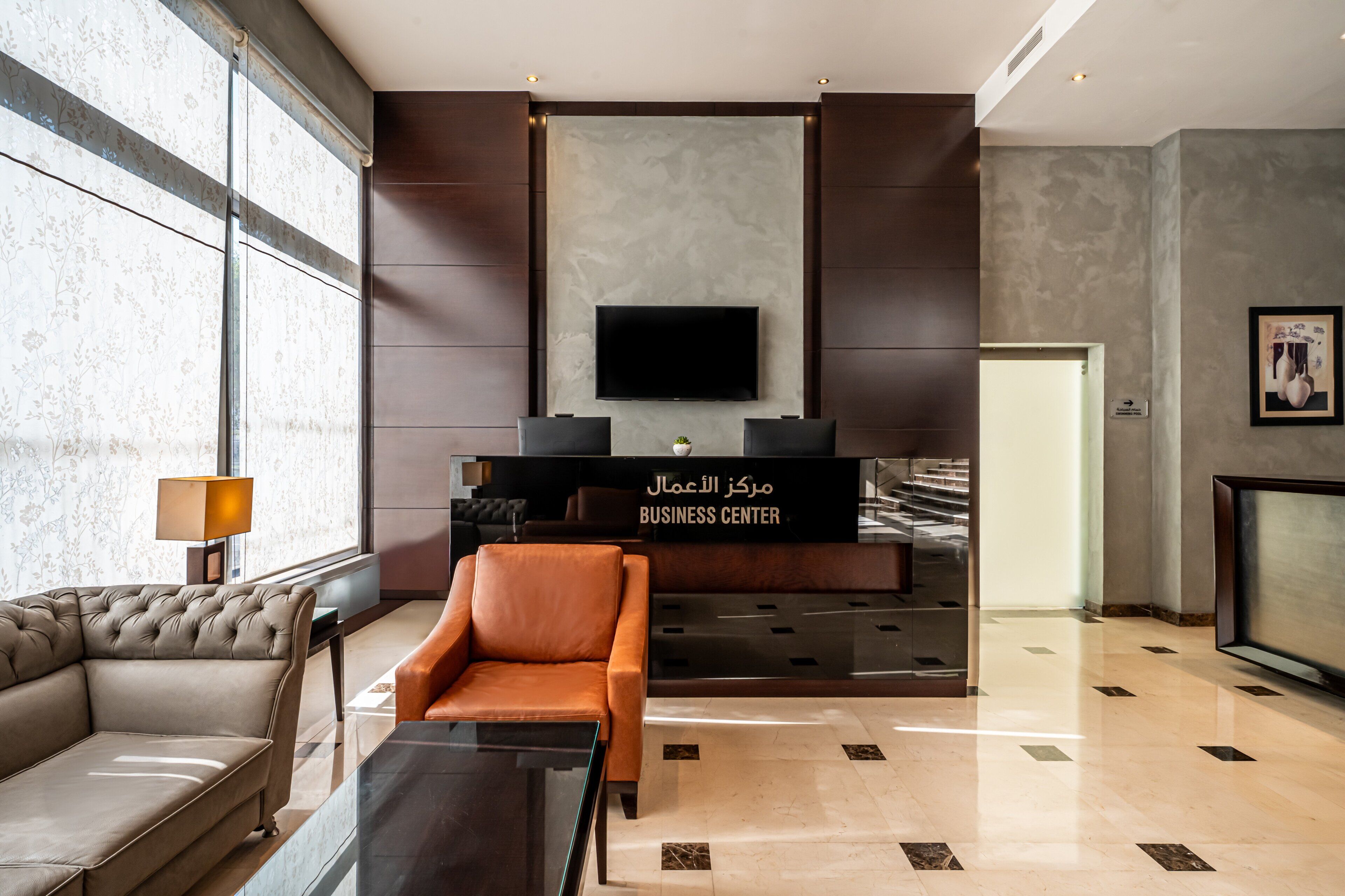A modern lobby with a sofa, armchair, and a reception desk labeled 'BUSINESS CENTER'.