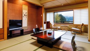 Un salón de estilo japonés tradicional con suelo de tatami, una mesa baja y puertas correderas que dan a un balcón con vistas a la montaña.