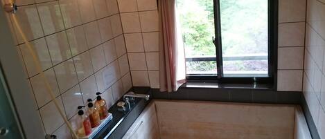 A bathroom with a bathtub, a shower, and a window with a view of greenery.