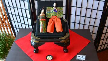 Una exhibición de muñecas japonesas tradicionales sobre una mesa con un paño rojo, frente a un panel con diseño de cuadrícula.