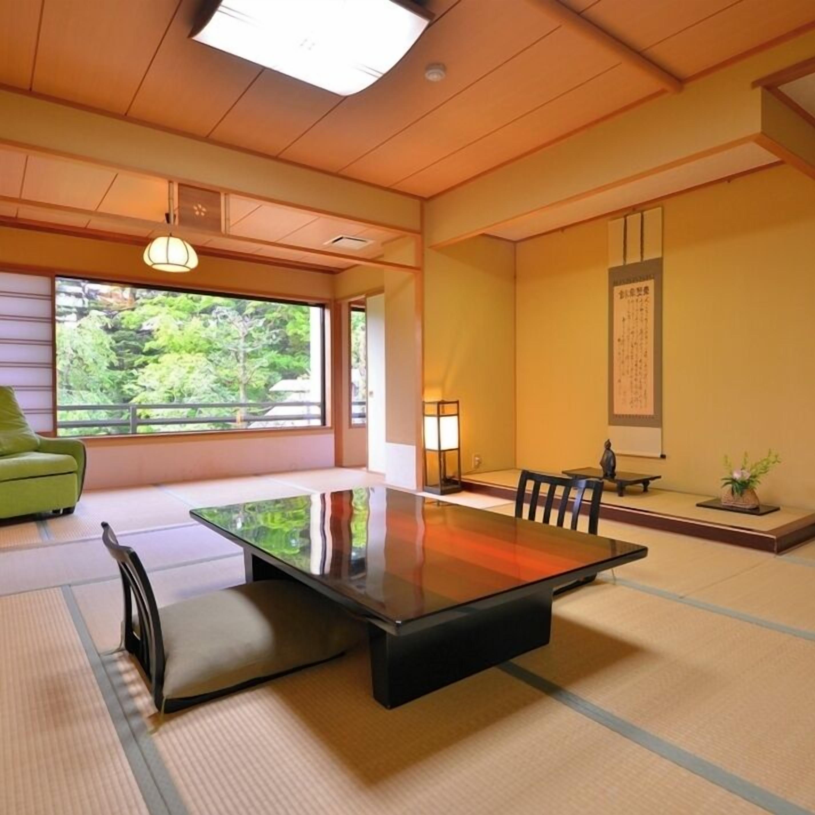 A traditional Japanese room with tatami flooring, a low table, a green sofa, and a view of greenery outside.