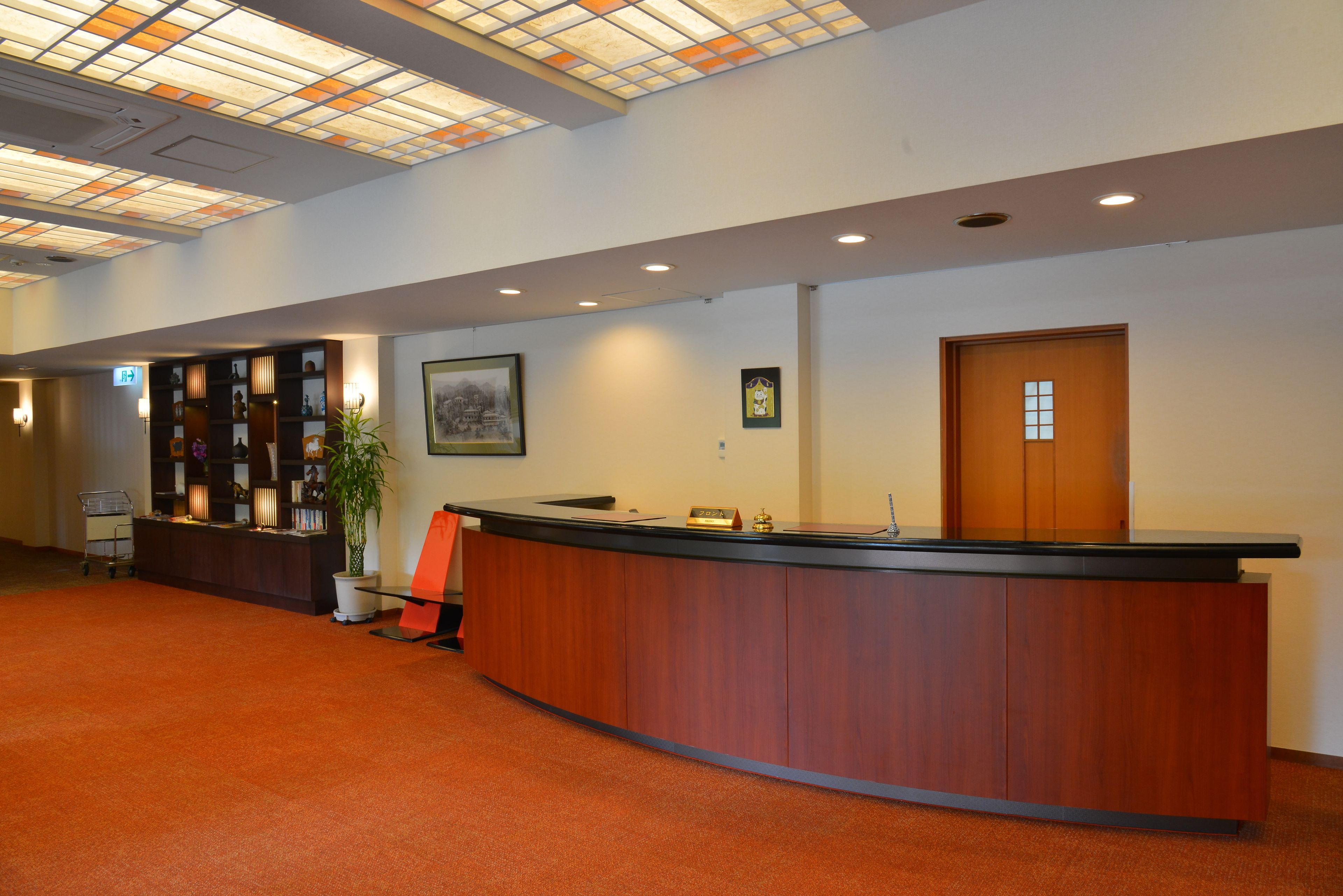 A reception area with a wooden reception desk, a potted plant, a framed picture on the wall, and a door.