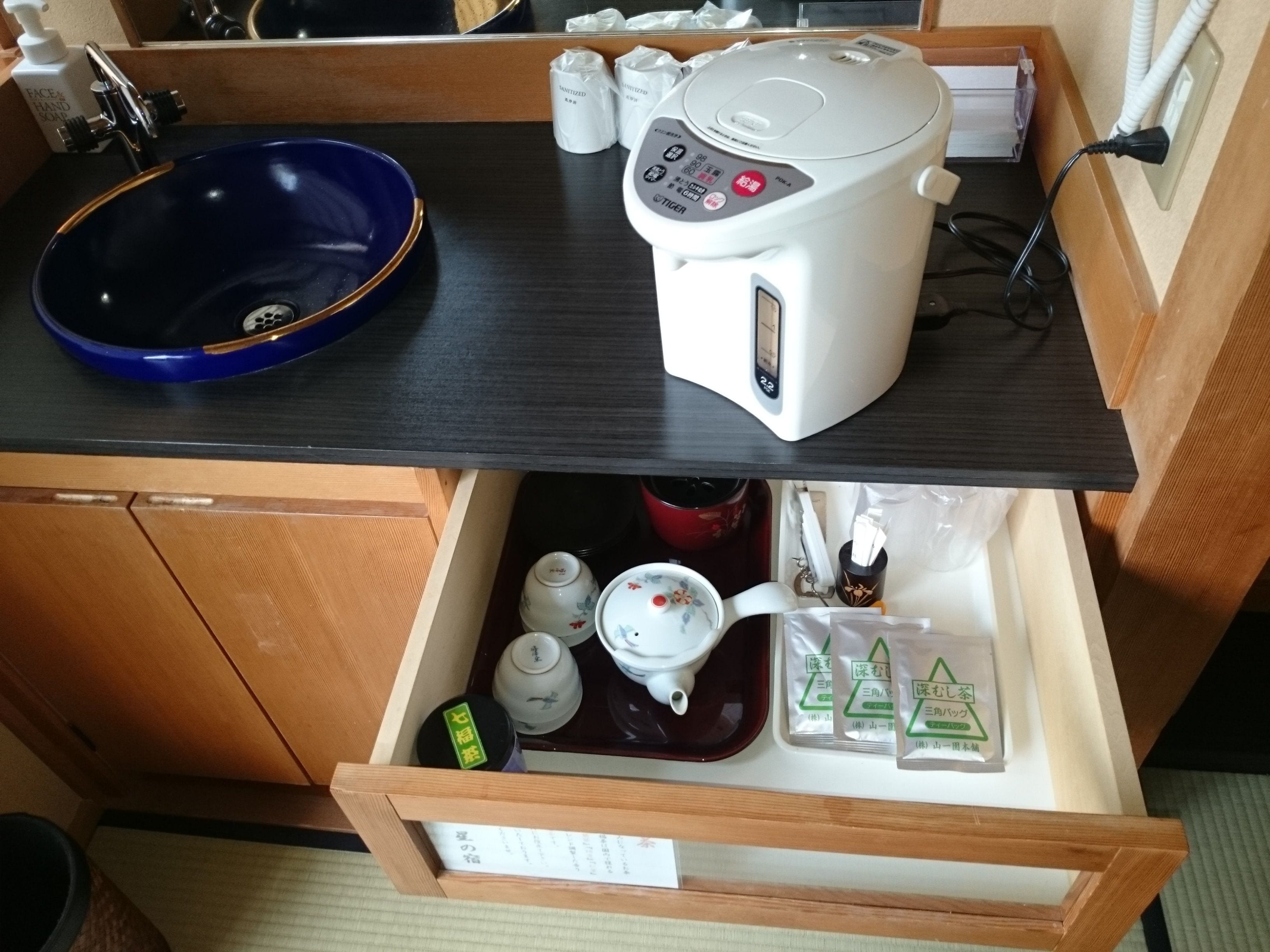 A kitchen counter with a blue bowl, a rice cooker, and a tea set.