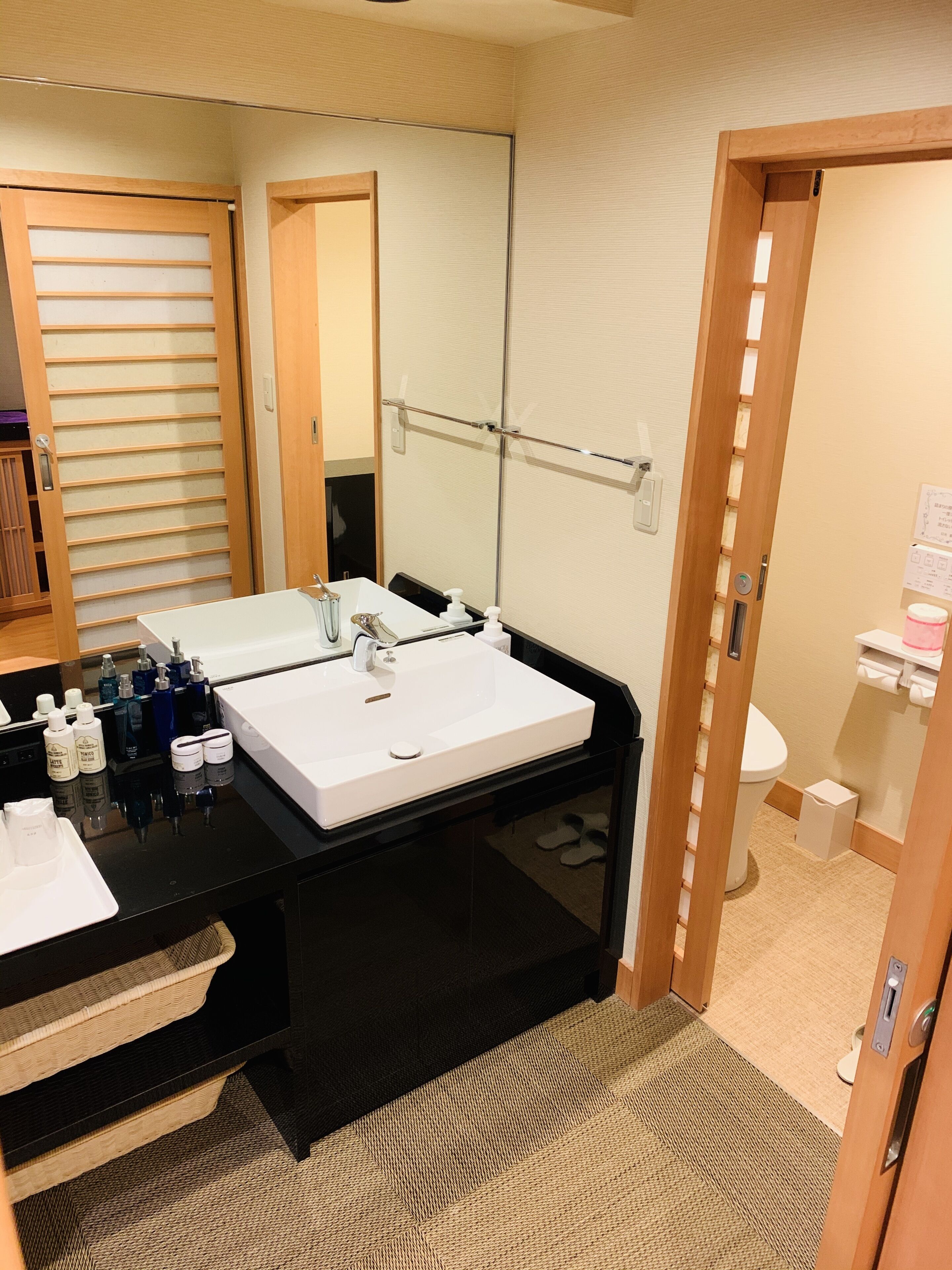 A hotel bathroom with a black vanity, two sinks, a large mirror, and a toilet.