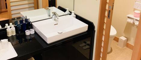 A hotel bathroom with a black vanity, two sinks, a large mirror, and a toilet.