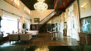 A spacious room with a grand staircase, wooden flooring, and classic furnishings including armchairs and a table with a vase. - Cadasa Resort Dalat (Xuan Huong - Da Lat)