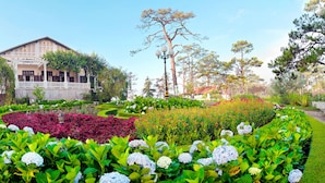 A large building with a covered porch, surrounded by well-maintained gardens with various plants and flowers. - Cadasa Resort Dalat (Xuan Huong - Da Lat)