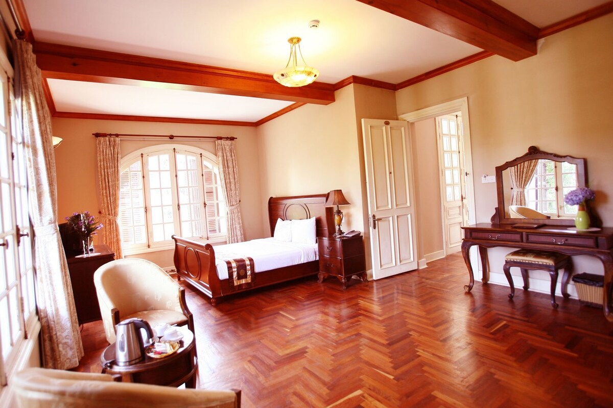 A room with a wooden floor, a bed, a chair, a dresser, and a mirror.