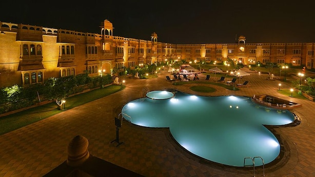 A large, illuminated swimming pool in the center of a courtyard with a grand building in the background. - Hotel Desert Tulip (Jaisalmer)