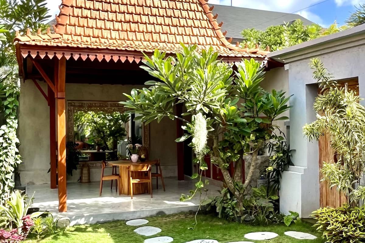 Ein Haus mit einem Ziegeldach, einem Schwimmbad und einem Garten mit verschiedenen Pflanzen.