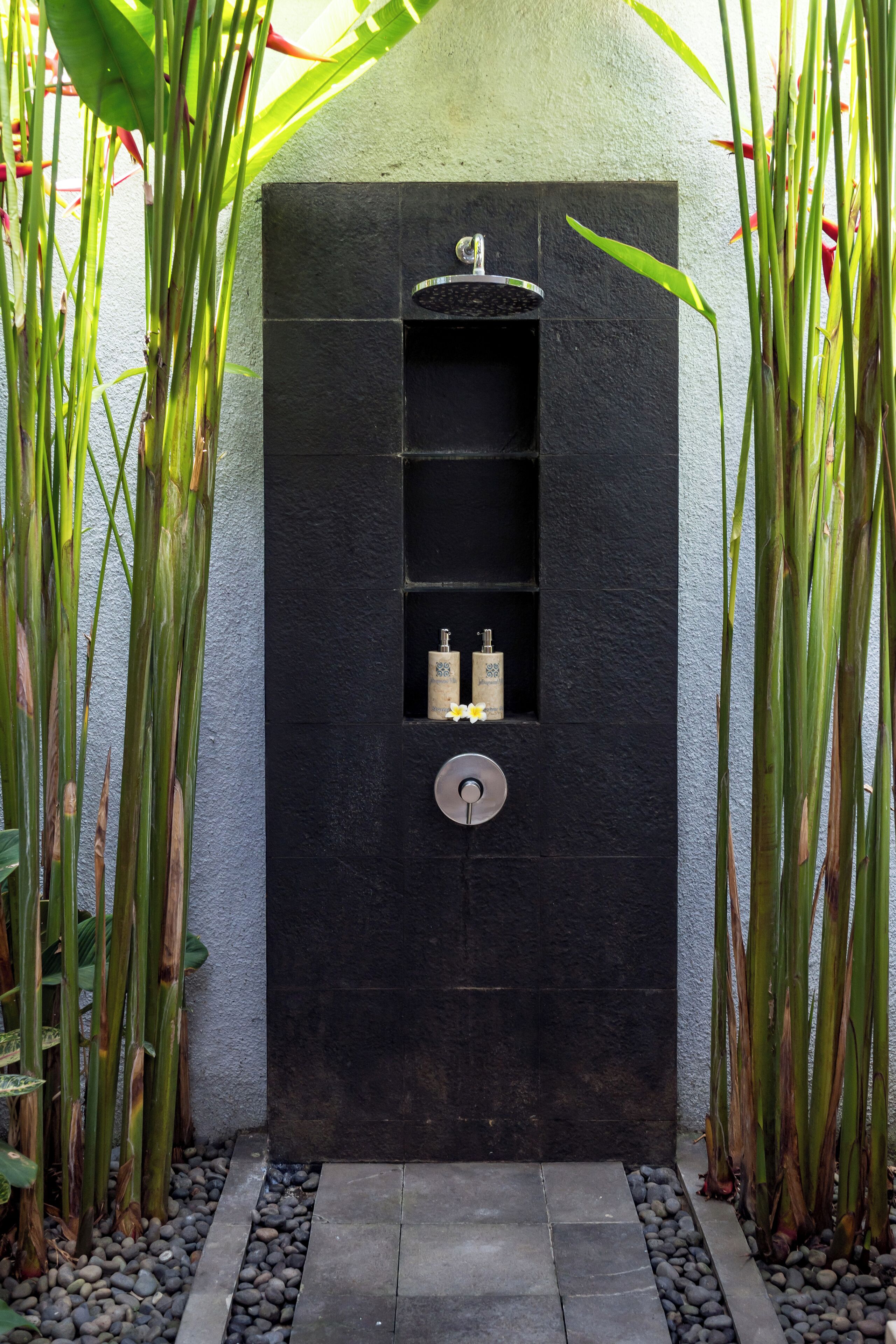 Een zwarte wand met een ingebouwd wastafelmeubel en plank, omringd door hoge planten.