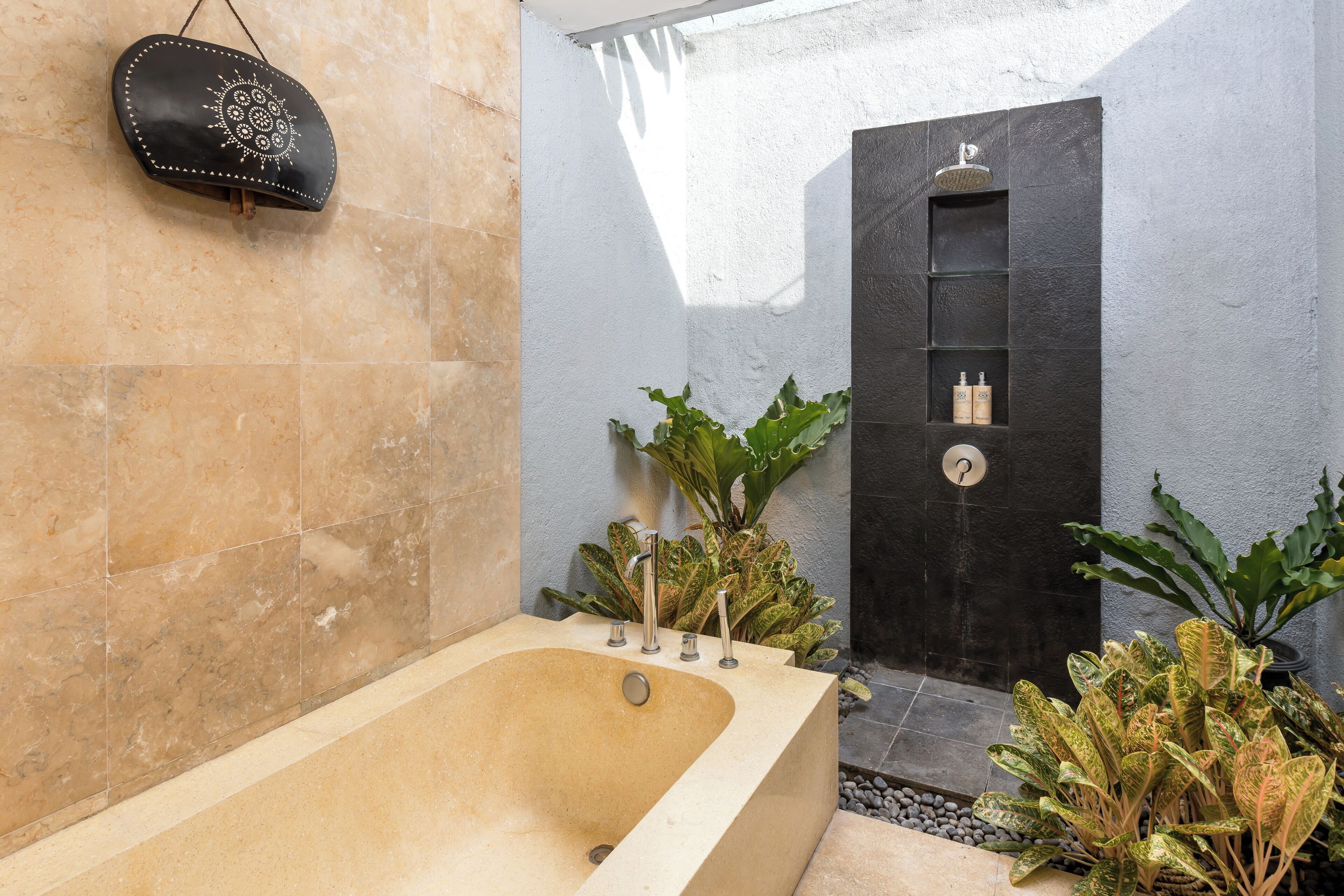 A modern bathroom with a freestanding bathtub, a black wall-mounted shelf with toiletries, and lush green plants.