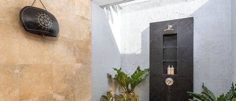 A modern bathroom with a freestanding bathtub, a black wall-mounted shelf with toiletries, and lush green plants.