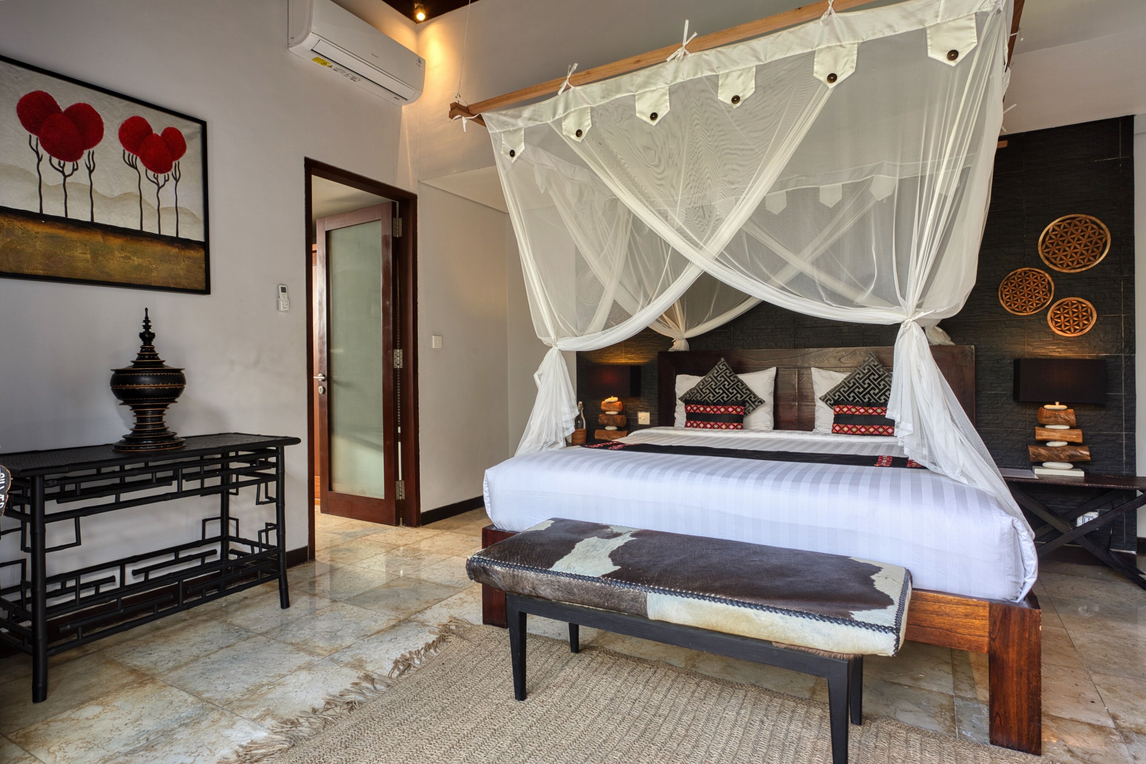A bedroom with a four-poster bed, a bench, a table, and a decorative wall piece.