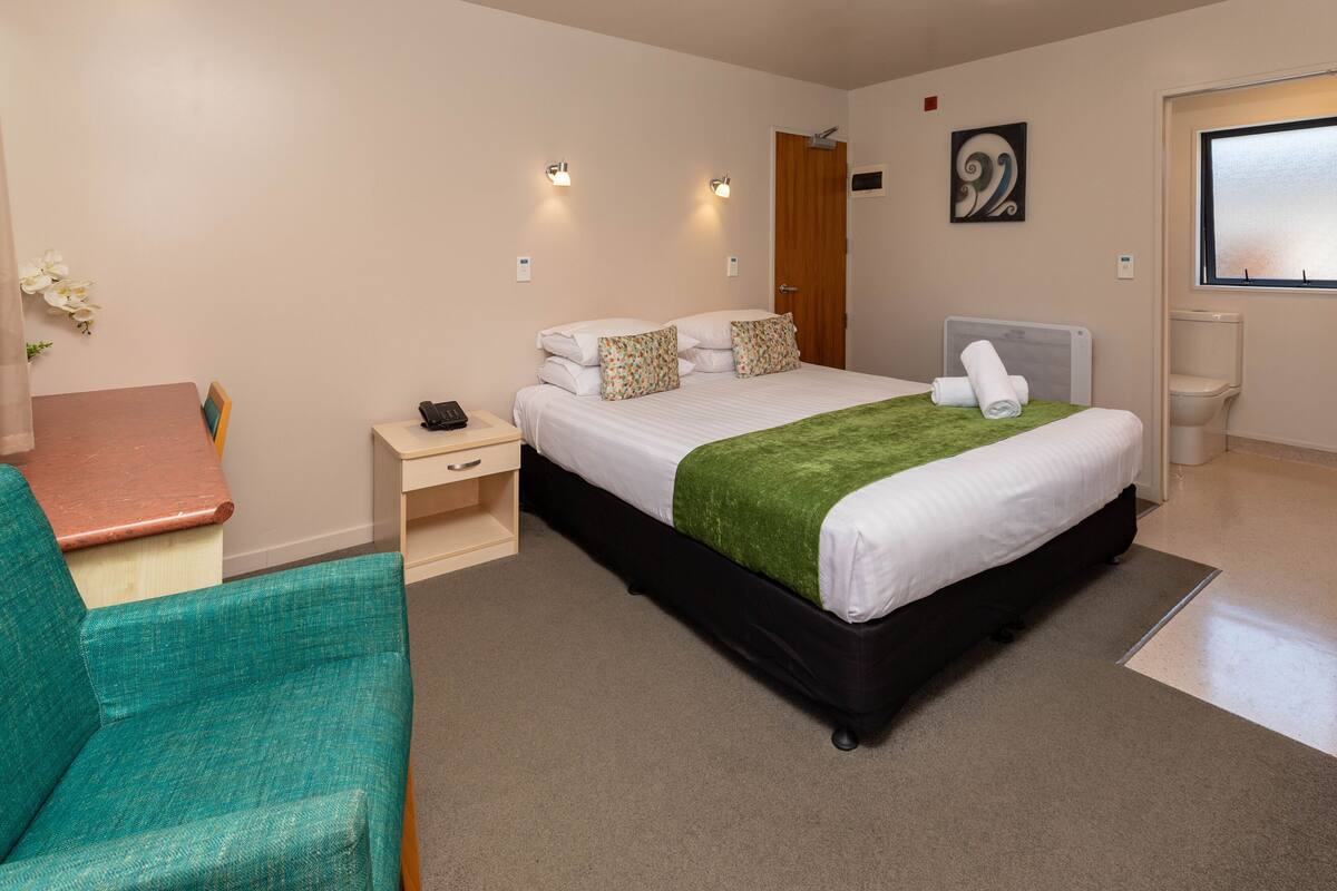 A bedroom with a bed, bedside table, chair, and a painting on the wall.
