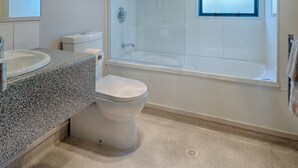 A modern bathroom with a granite countertop, a toilet, a glass-enclosed shower, and a window.