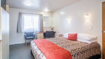 Quarto de hotel com cama, secretária, cadeira, guarda-roupa e janela com cortinas.