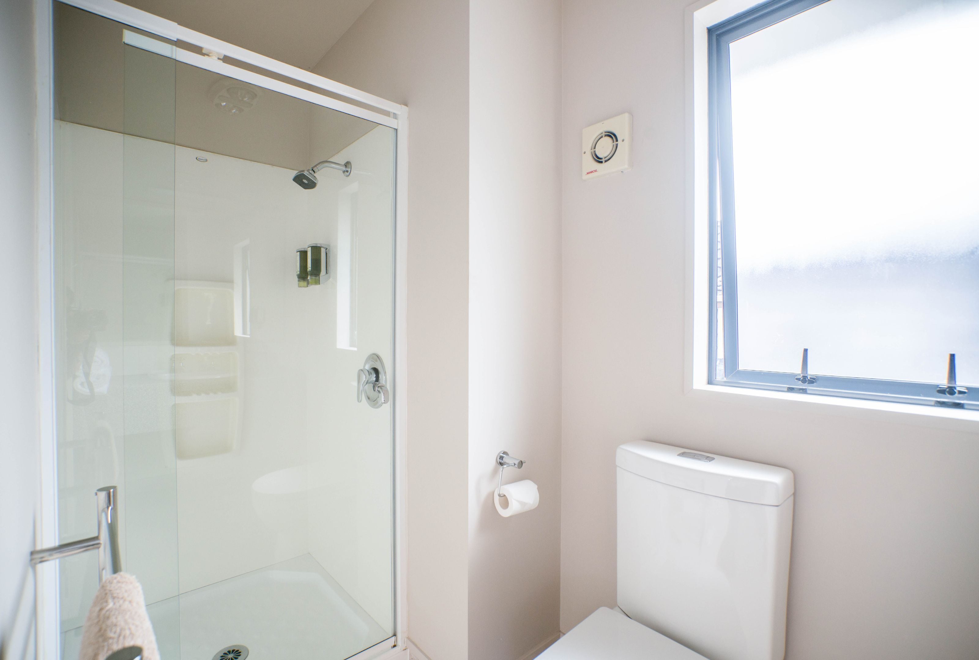 Ein Badezimmer mit Duschkabine aus Glas, Toilette und Fenster.