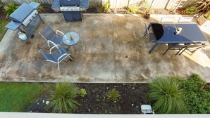 A backyard patio with a grill, a table, chairs, and a small garden area.