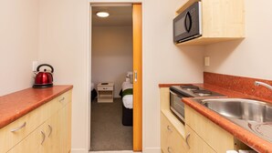 A compact kitchen with wooden cabinets, a red kettle, a microwave, and a sink.