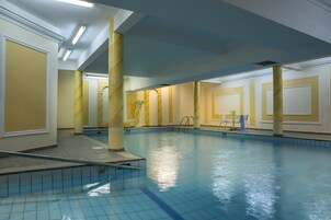 A swimming pool with a tiled floor and walls, a marble column, and a small table with chairs.