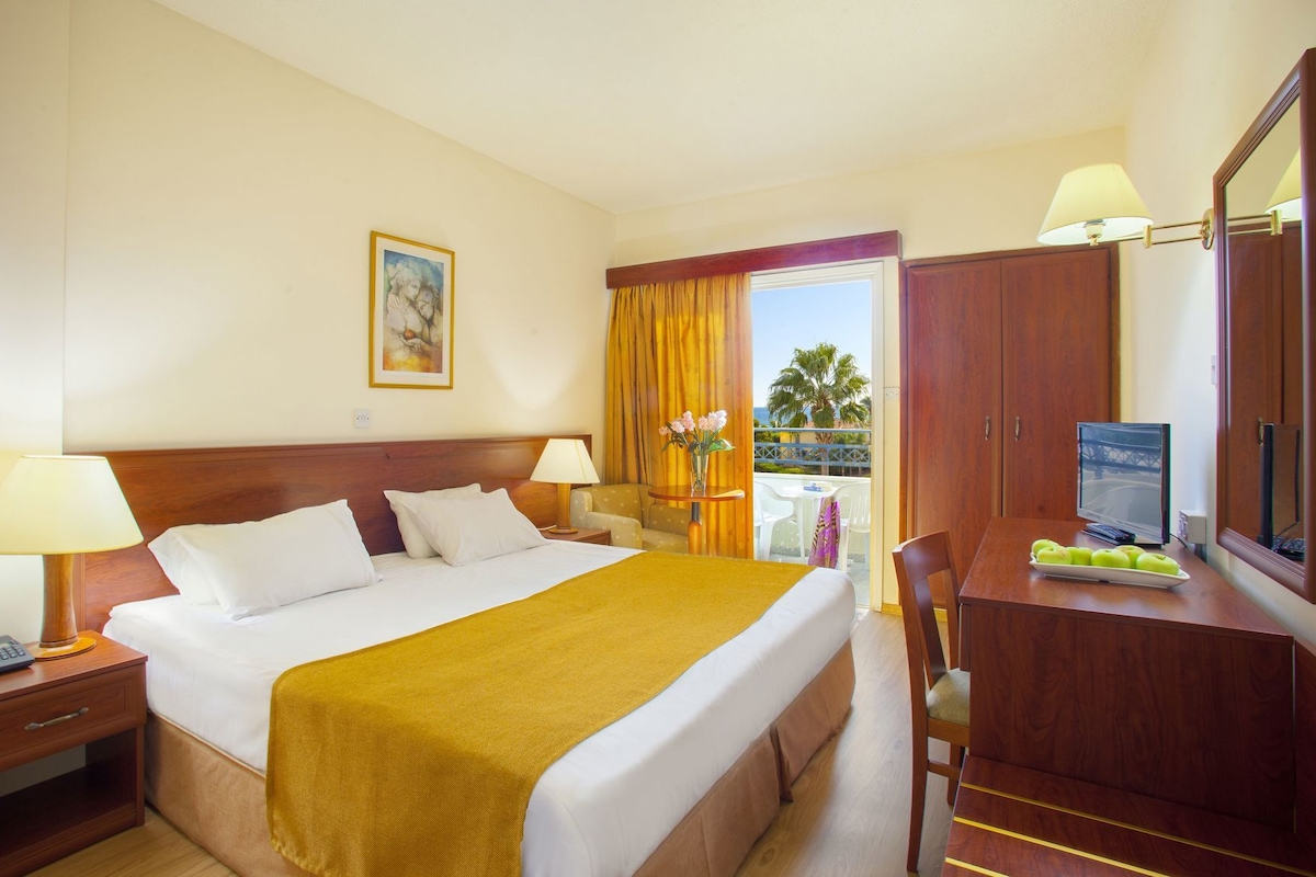 A hotel room with a bed, bedside lamps, a desk with a computer, and a view of the outdoors.
