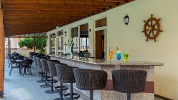 A covered outdoor bar area with wicker bar stools and a counter.