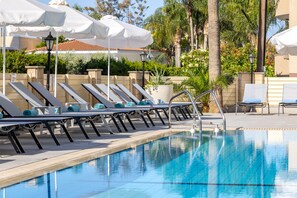 A poolside area with lounge chairs and umbrellas, surrounded by greenery and palm trees. - Kapetanios Limassol Hotel (Limassol)
