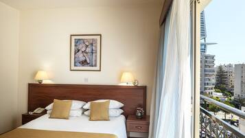 Une chambre d’hôtel avec un grand lit, deux lampes de chevet, une œuvre d’art encadrée au mur et une vue sur la ville par la fenêtre.