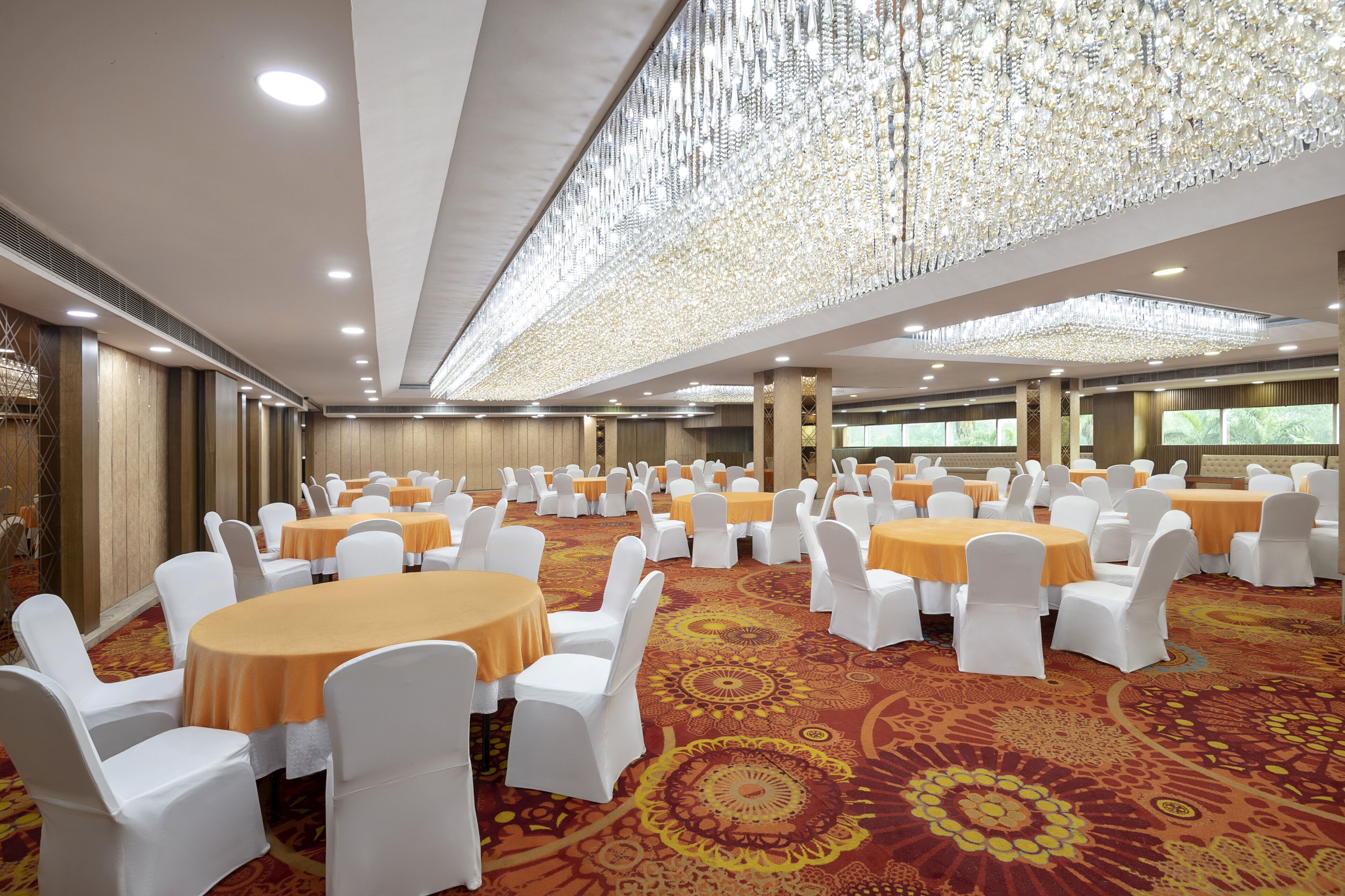 Une salle de banquet avec des tables rondes, des chaises blanches et un tapis à motifs.