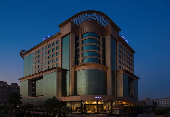 Hotel features a distinctive curved glass facade and a prominent entrance with illuminated signage.