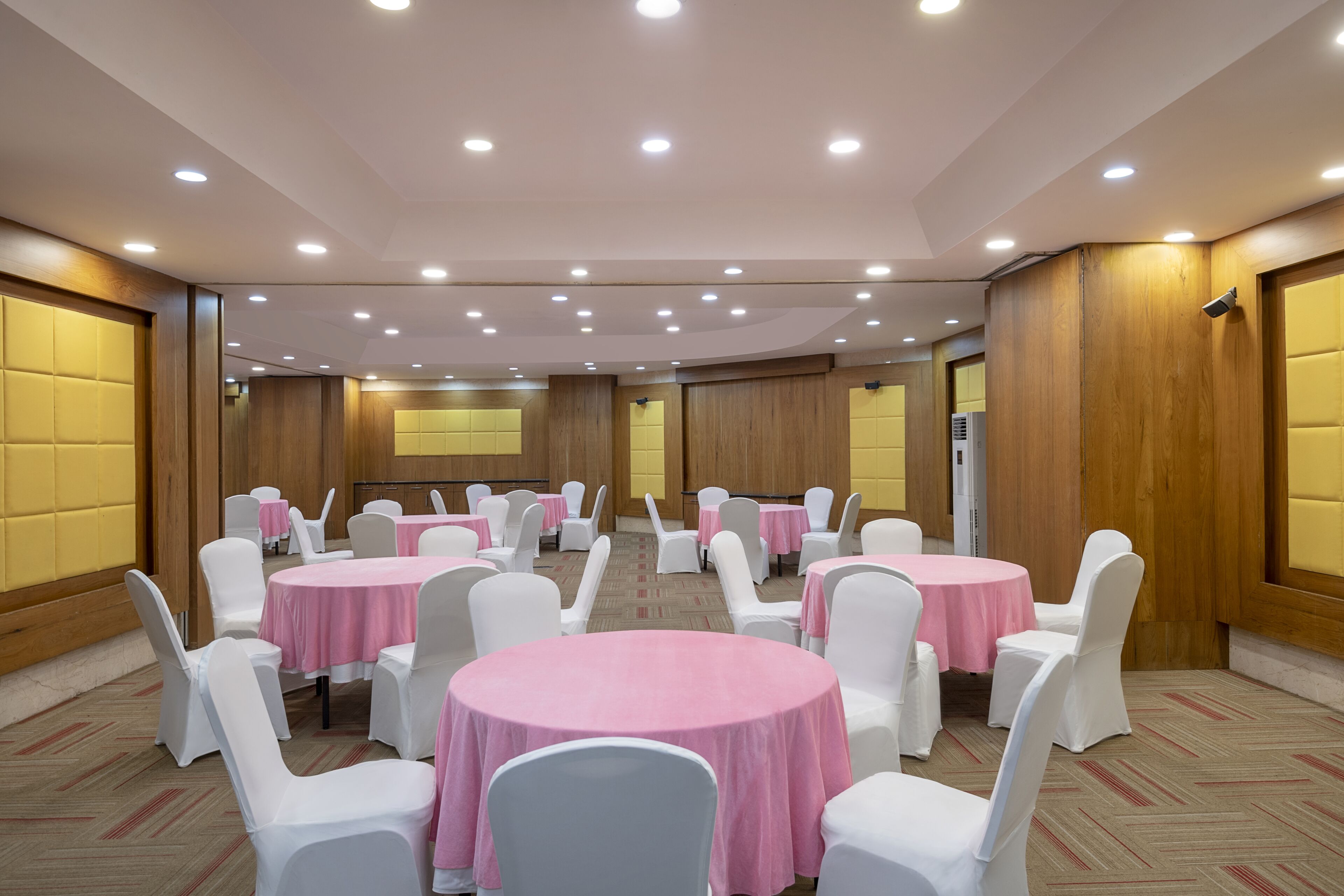 A conference room with round tables, white chairs, and pink tablecloths.