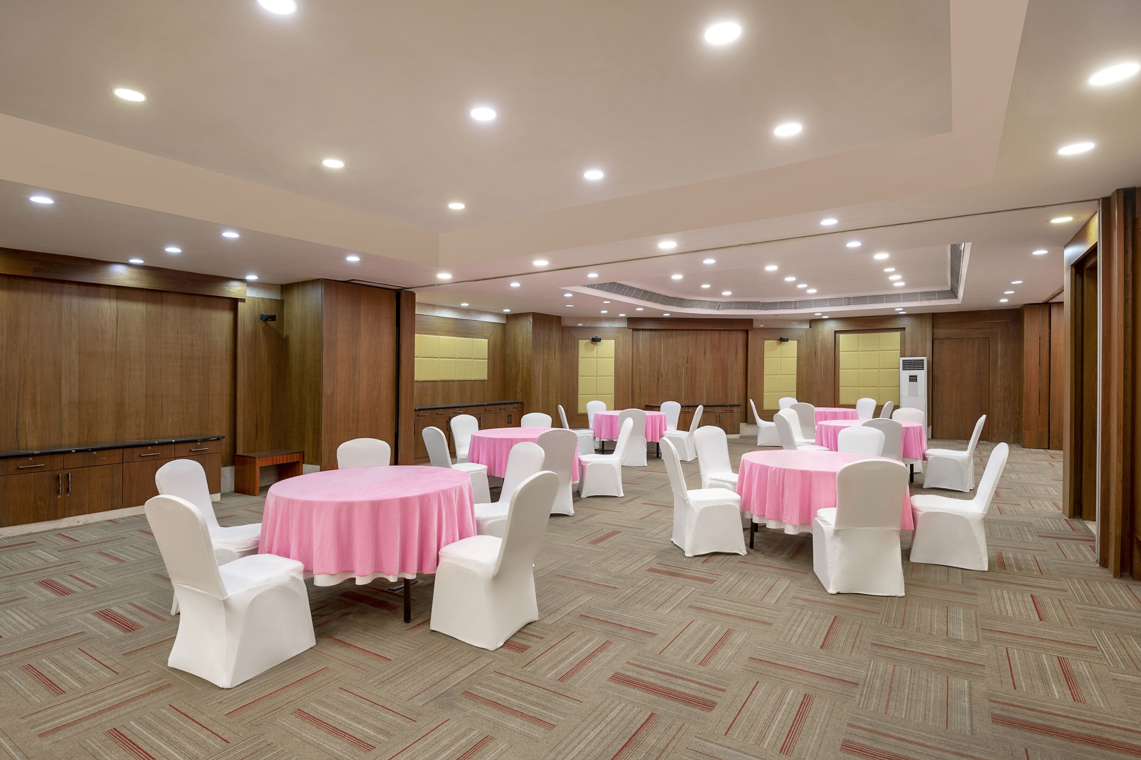 Une salle de conférence avec des tables rondes, des chaises blanches et des nappes roses.