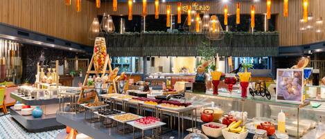 A buffet area with various food items and a salad bar, under a modern ceiling with hanging lights.