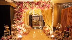 Een weelderige entree met een bloemrijke boog, gouden gordijnen en decoratieve verlichting.