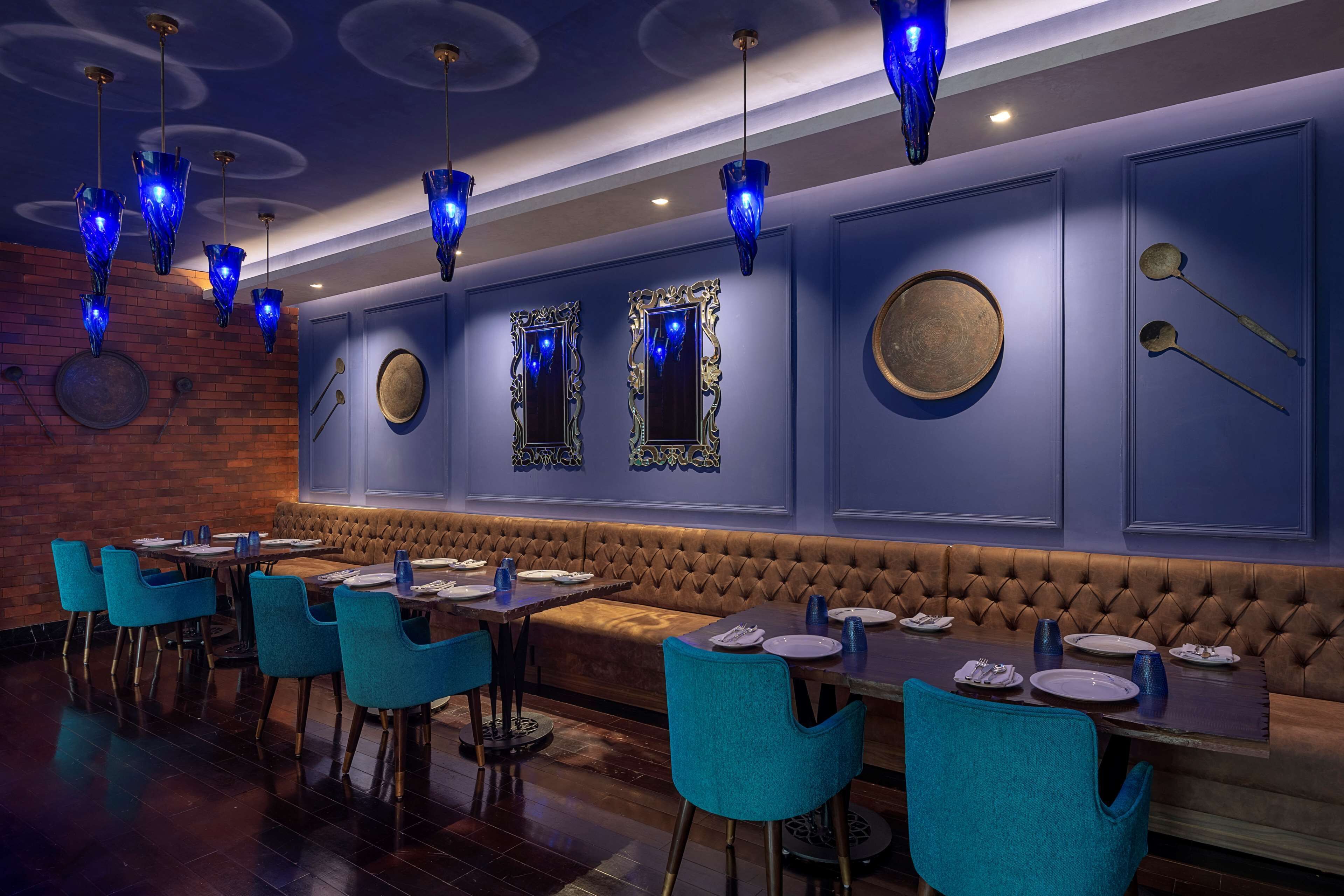 A restaurant with blue chairs, a brown cushioned bench, and blue pendant lights.