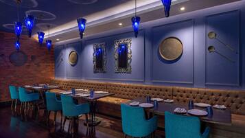 A restaurant with blue chairs, a brown cushioned bench, and blue pendant lights.