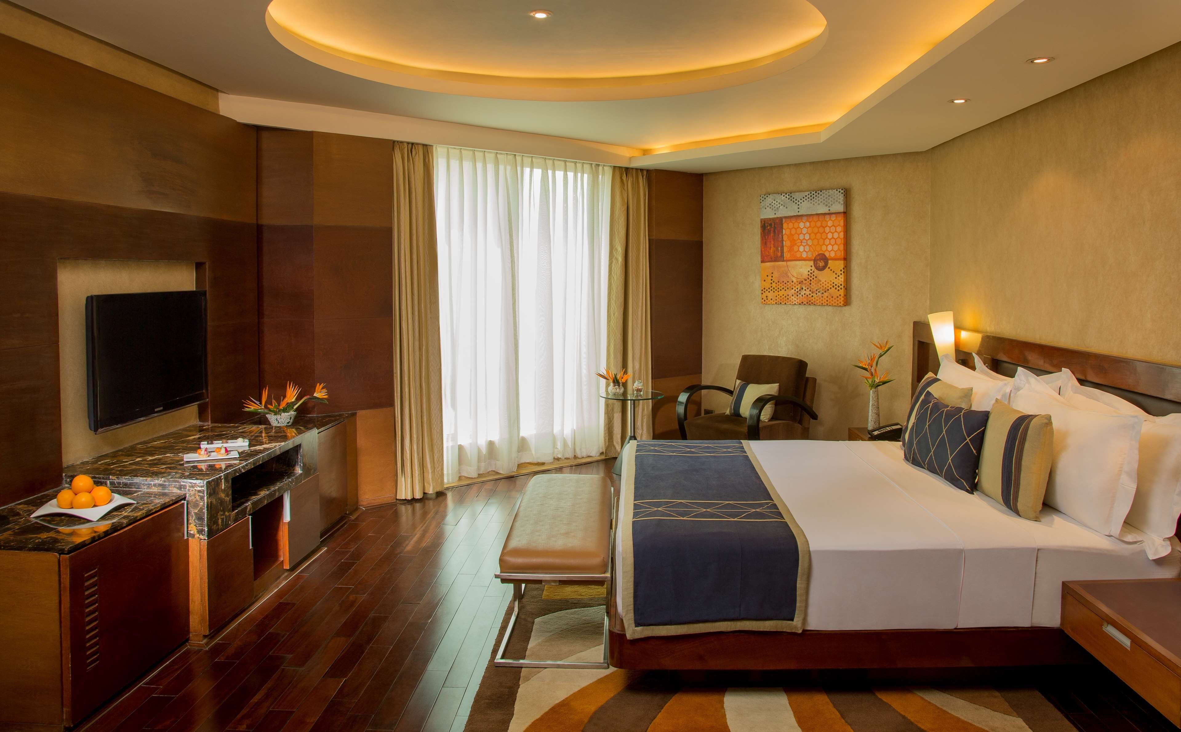 A hotel room with a bed, bedside table, TV, and a desk with a chair.