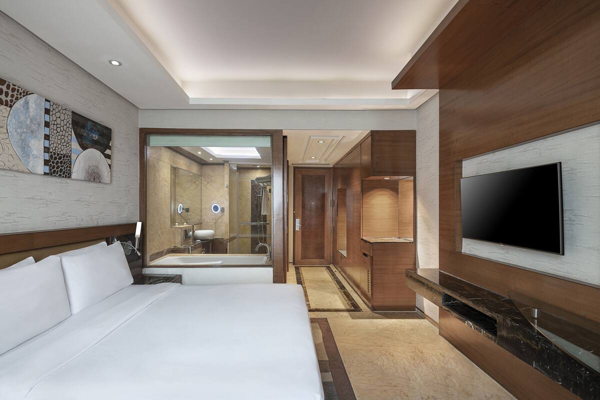 Een hotelkamer met een groot bed, een aan de muur bevestigde televisie, een spiegel en een inloopkast.