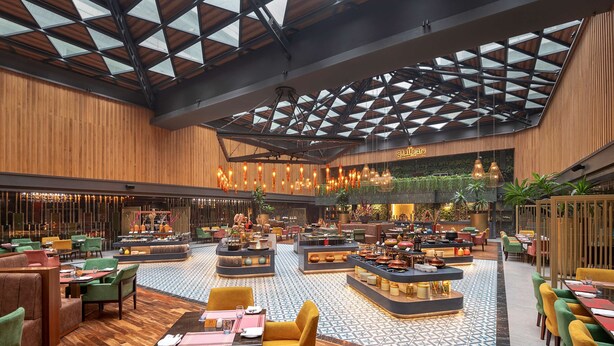 Een ruime lobby met een hoge plafond, houten lambrisering en een centraal zitgedeelte met meerdere tafels en stoelen.