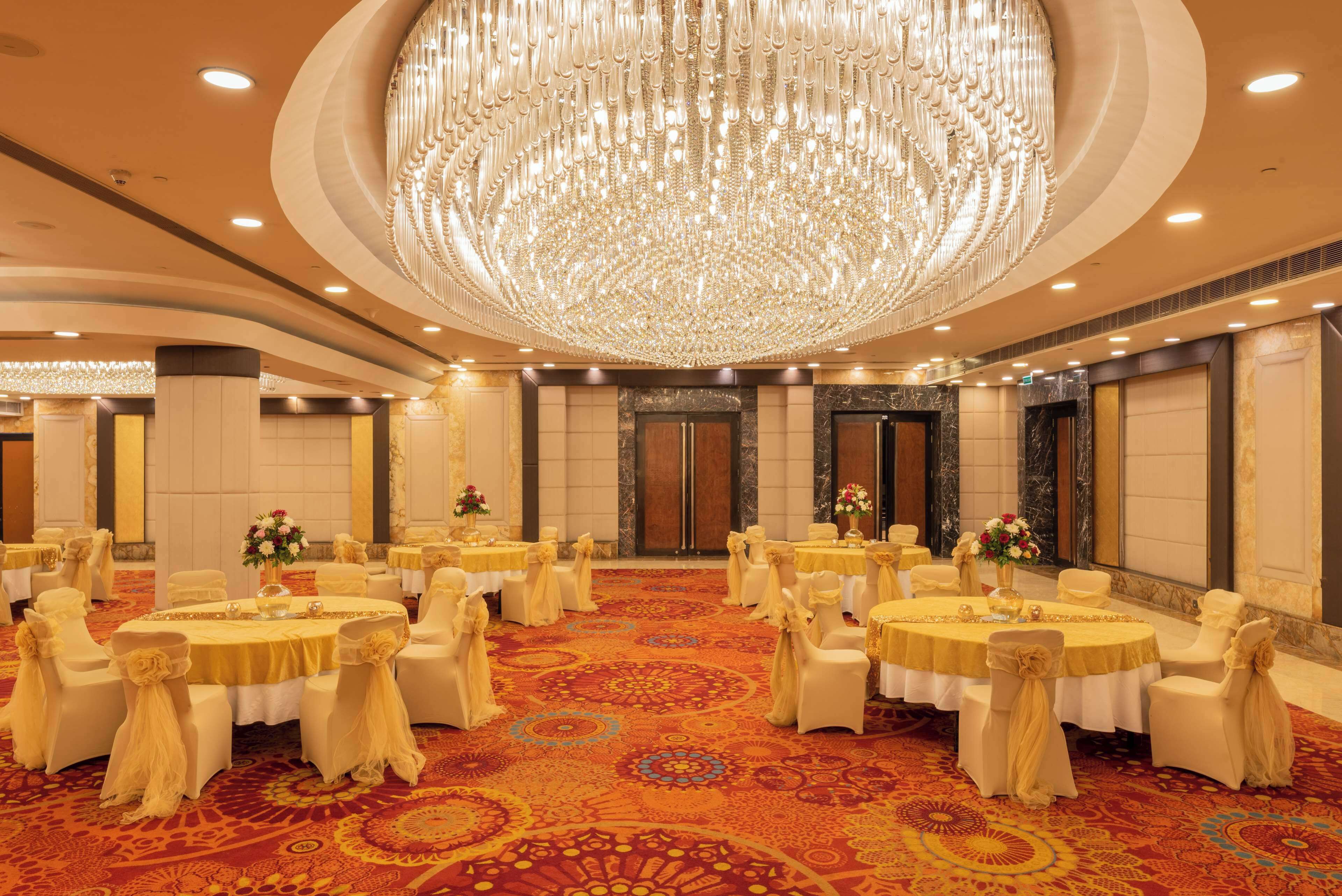 Une salle de banquet avec des tables rondes, des chaises blanches et un grand lustre.