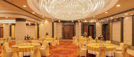 Une salle de banquet avec des tables rondes, des chaises blanches et un grand lustre.