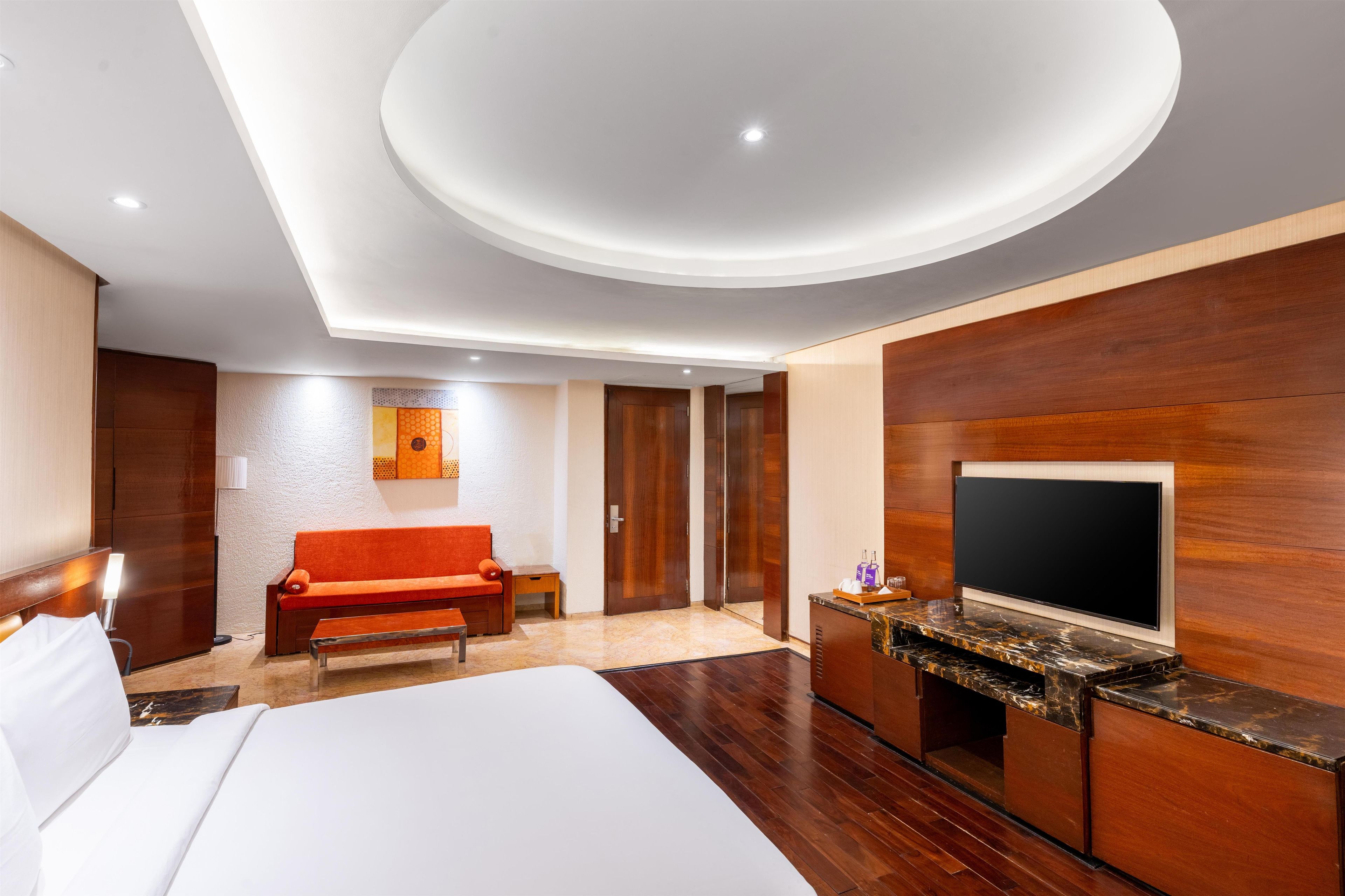 A modern hotel room with a large bed, a sofa, a TV, and a desk with a marble top.