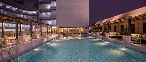 A pool area with a long, narrow pool, lounge chairs, and a bar area.