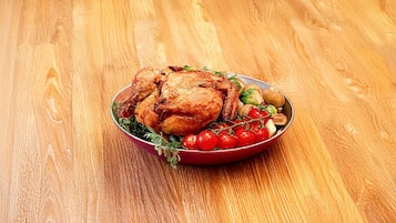 A roasted chicken on a plate with vegetables and herbs, placed on a wooden table.